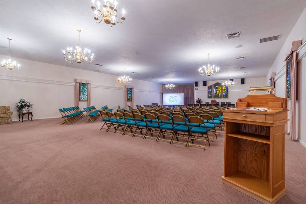 Empty church hall with rows of blue chairs, pulpit, and chandeliers under a white ceiling