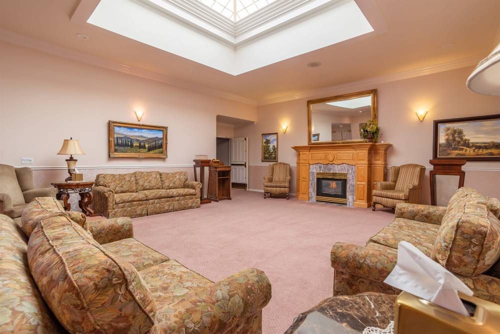 Spacious living room with tan sofas, pink carpet, skylight, and a fireplace centered on the far wall