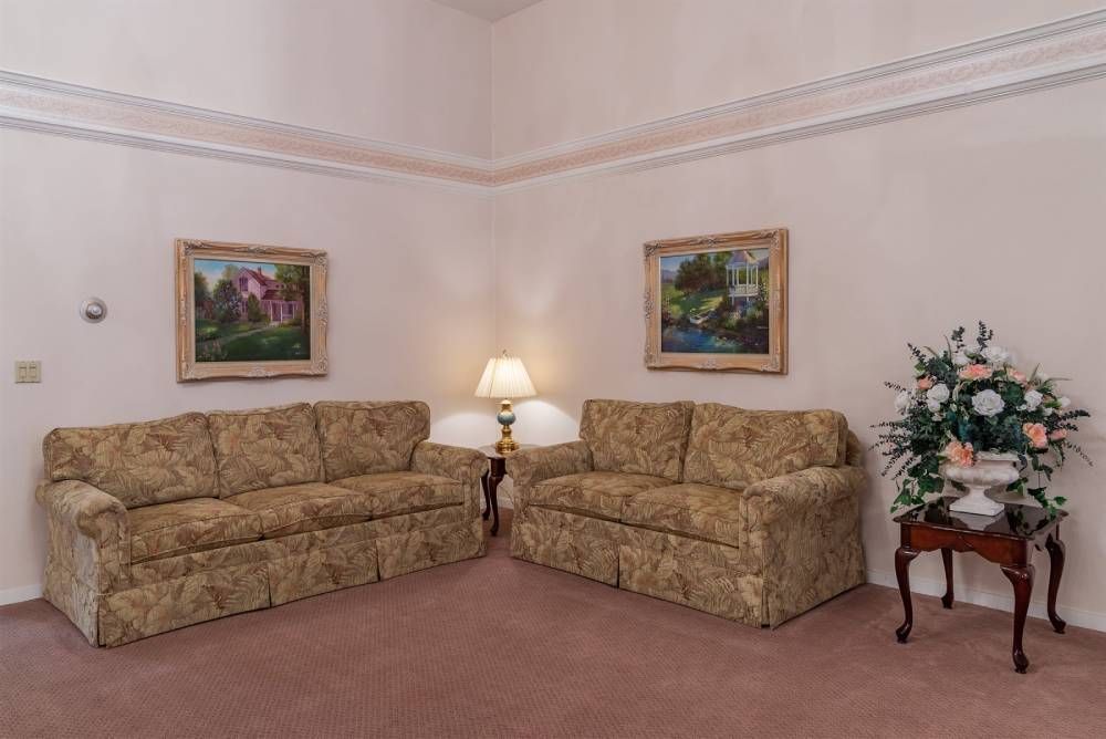 Living room with two beige sofas, framed art, a lamp, and a floral arrangement on a side table.