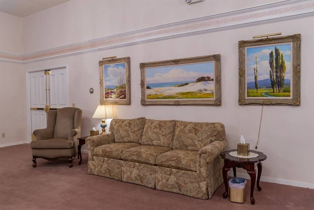 Living room with beige sofa, armchair, side table, and landscape paintings on white walls
