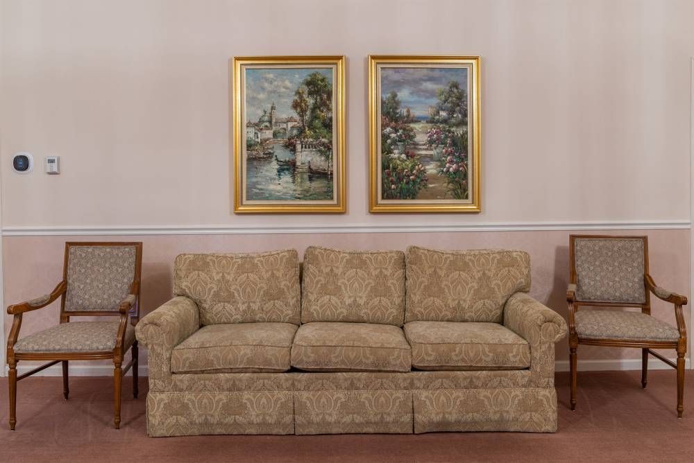 Beige sofa centered between two wooden chairs beneath two framed landscape paintings in a living room