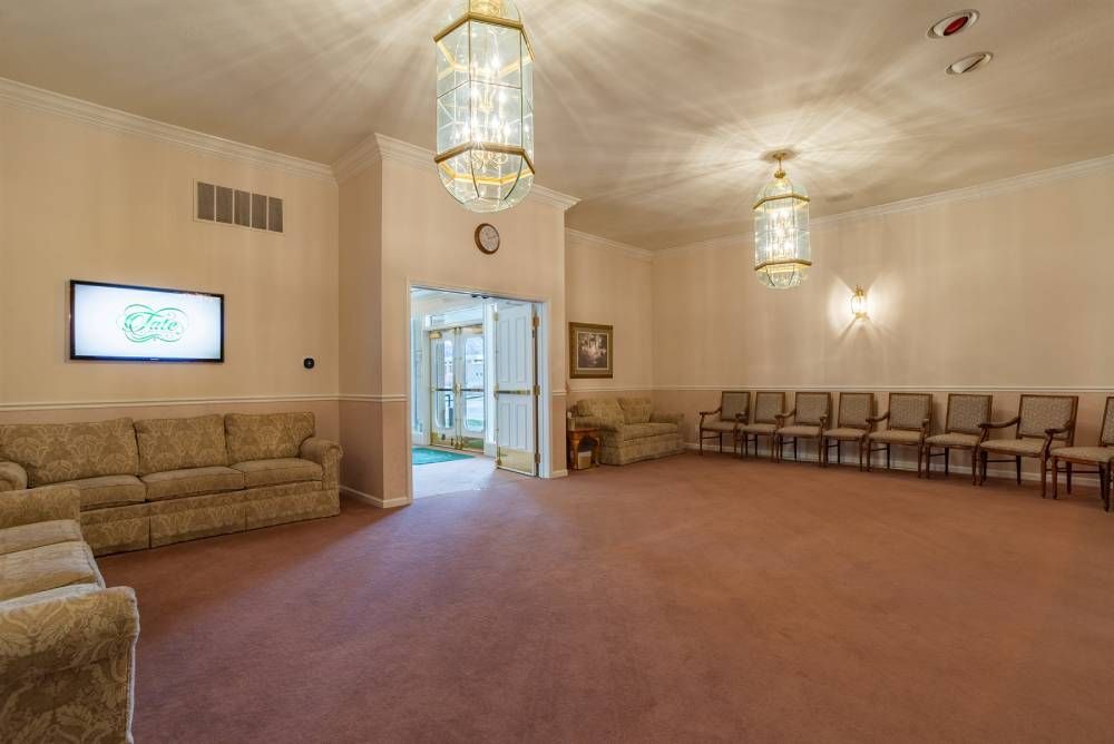 Spacious waiting room with beige carpet, sofa, rows of chairs, and pendant lights.