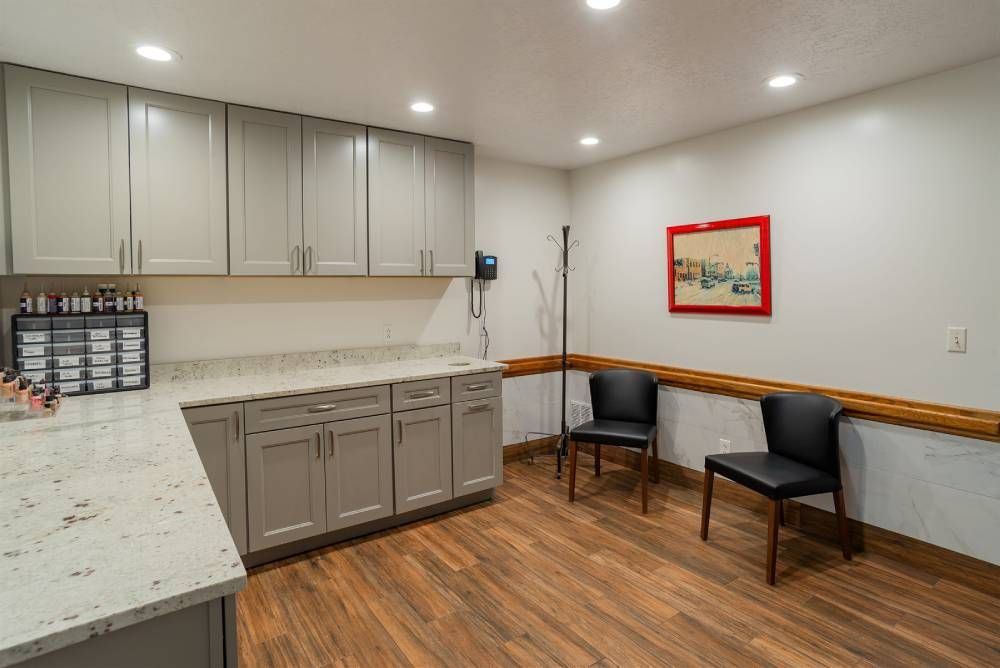 Small office break room with gray cabinets, wood floor, two chairs, and a framed wall picture.