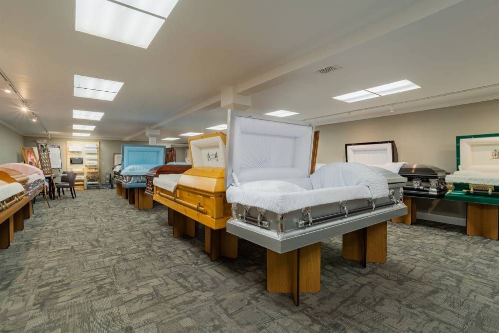 Funeral showroom with several caskets displayed under bright ceiling lights.