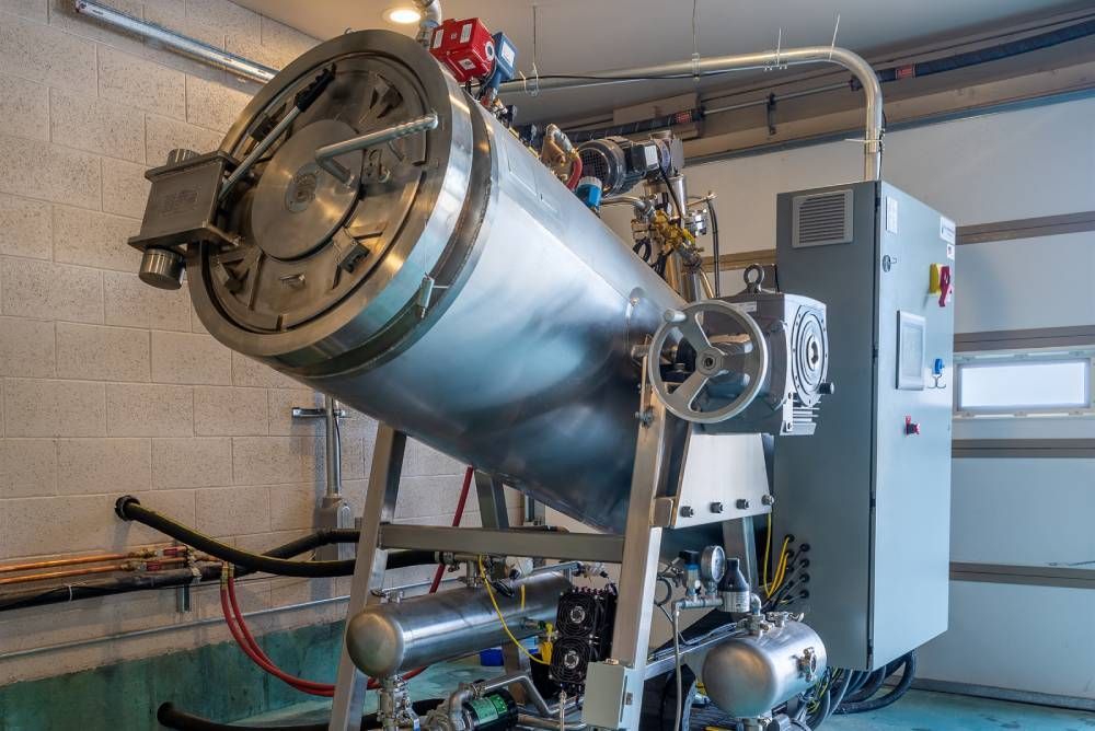 Industrial stainless steel cylindrical tank with pipes and valves in a utility room