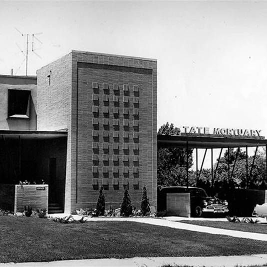 Black-and-white exterior of the Tate Mortuary building with entrance canopy and lawn