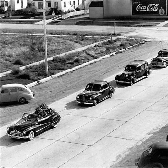 Black-and-white street scene with a parade of vintage cars and a Coca-Cola billboard in the background