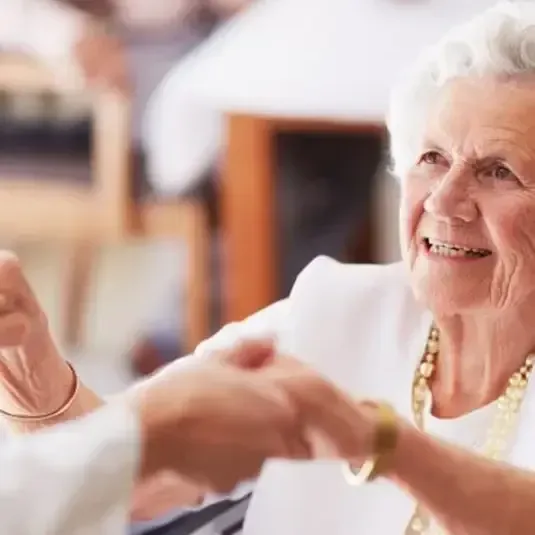Elderly woman smiling and dancing with a partner in a warmly lit room
