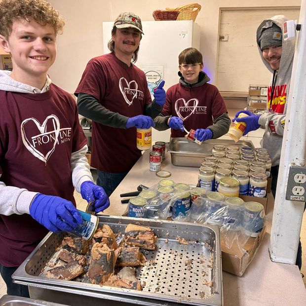 Three volunteers in maroon shirts grilling food outdoors at a community event