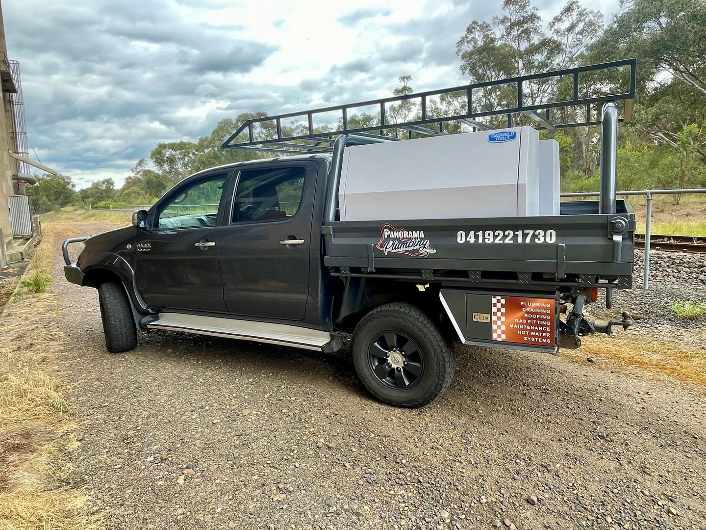 A black truck with a white tank on the back is parked on a gravel road — Panorama Plumbing In Dubbo, NSW