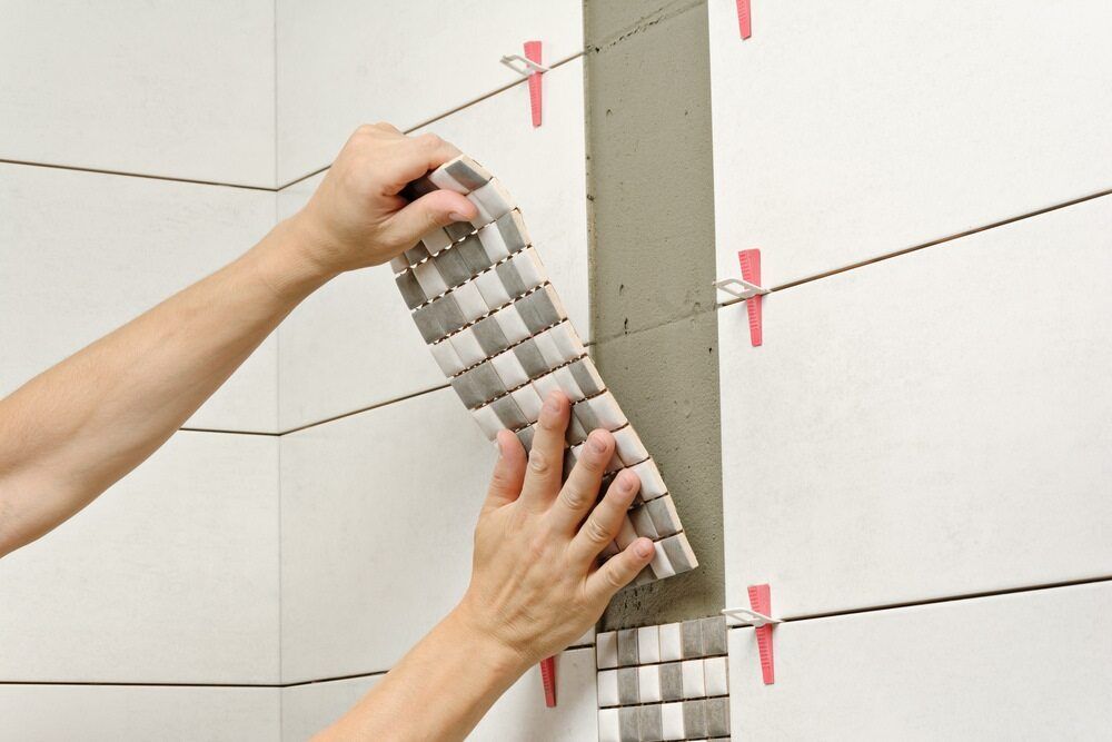 A Person Is Installing Tiles On A Wall — Panorama Plumbing In Dubbo, NSW