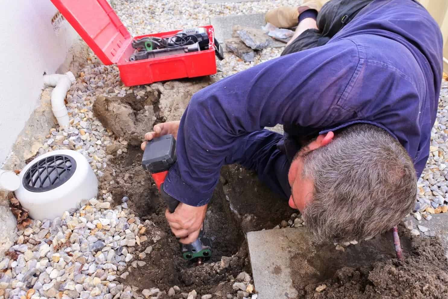 A Man Is Laying On The Ground Working On A Pipe — Panorama Plumbing In Dubbo, NSW