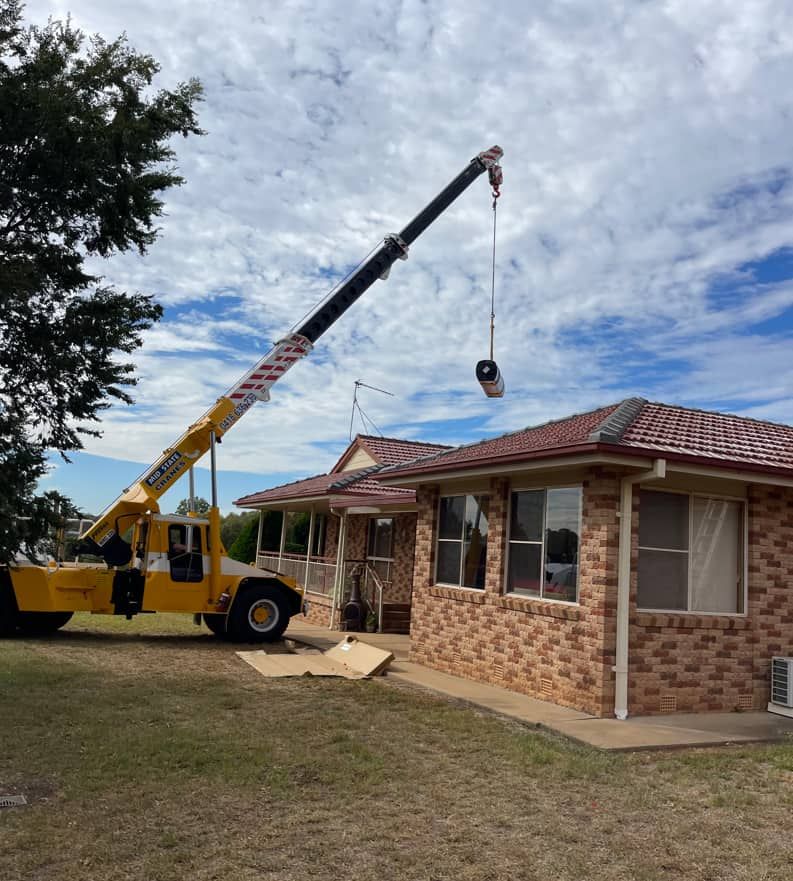 A Yellow Truck With A Crane Attached To It Is Parked In Front Of A House — Panorama Plumbing In Dubbo, NSW