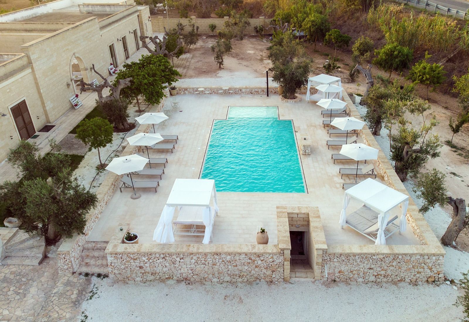 Vista a bordo piscina di un hotel con piscina turchese, cabine bianche ed edifici beige sotto un cielo soleggiato.