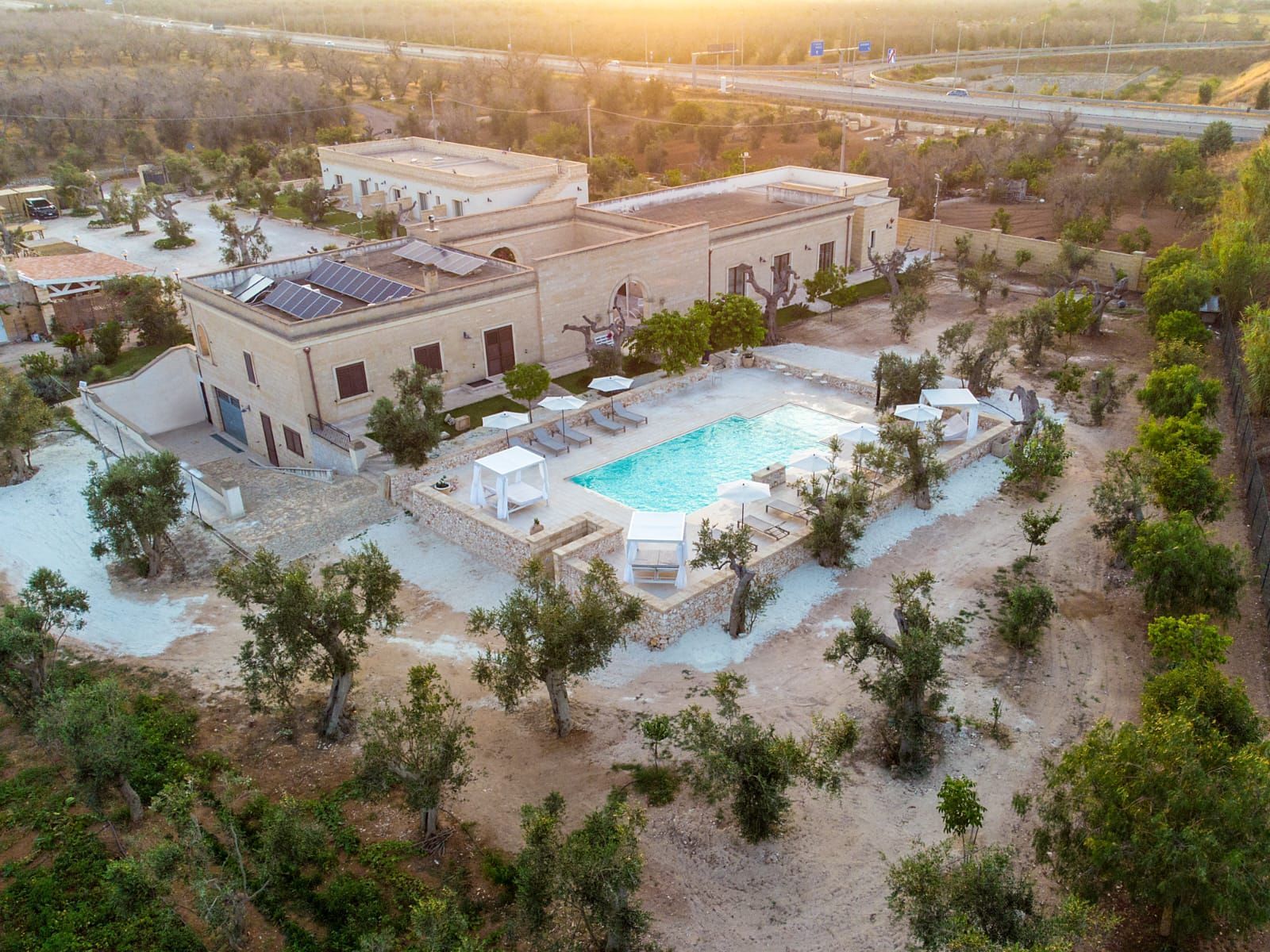 Vista aerea di un hotel con piscina, circondato da ulivi in ​​un ambiente soleggiato.