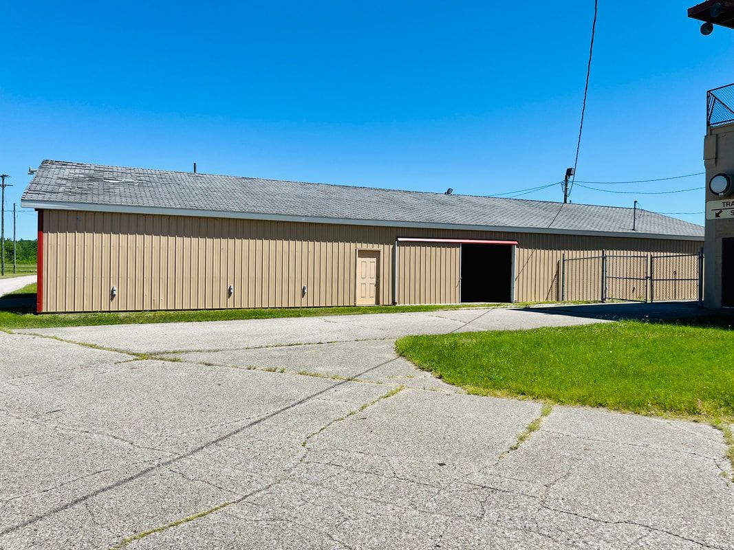 A large building with a sliding door is sitting in the middle of a grassy field.