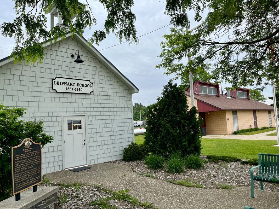 A small white building with a sign on the side of it and a bench in front of it.