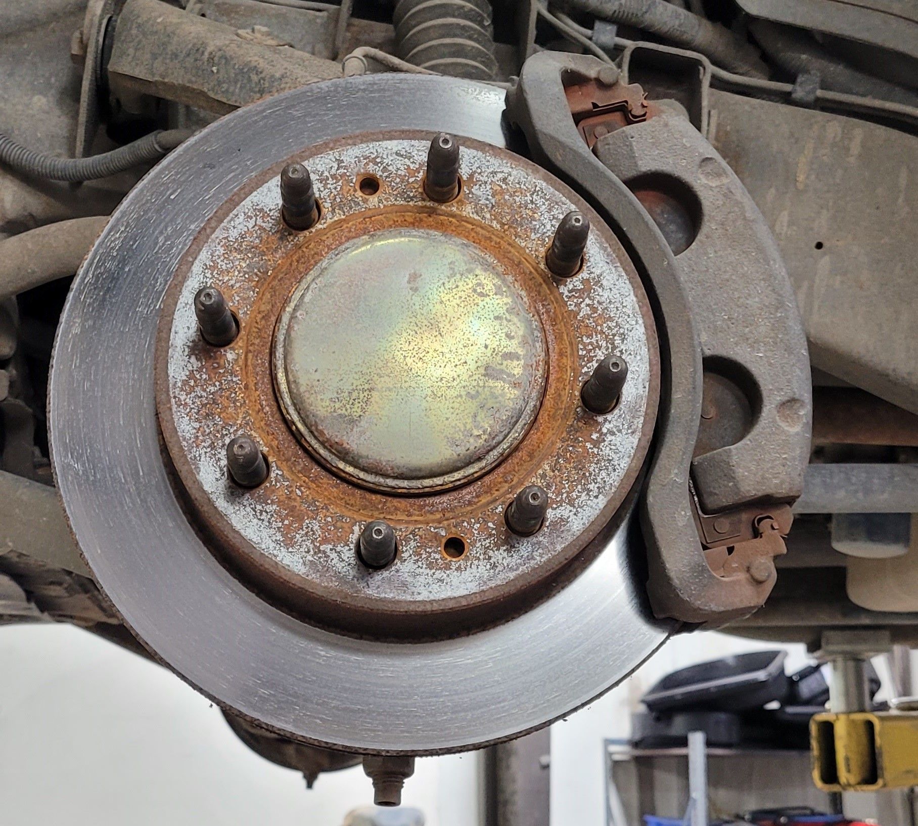 Close-up of a car brake rotor and rusty wheel hub with lug bolts and caliper assembly.