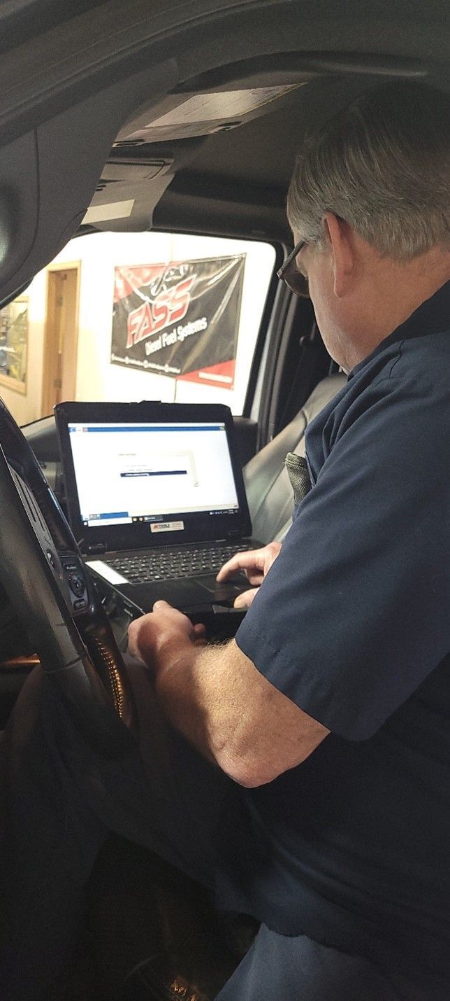Man leaning into a car, using a laptop on the center console in a dim interior.