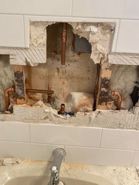 A bathroom sink with a hole in the wall and copper pipes coming out of it.