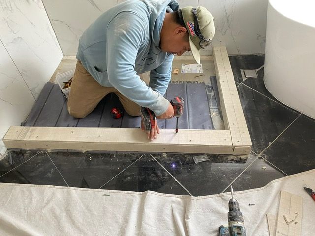 A man is kneeling down in a bathroom with a drill.