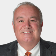 Eric Devlin in a suit and tie is smiling for the camera .