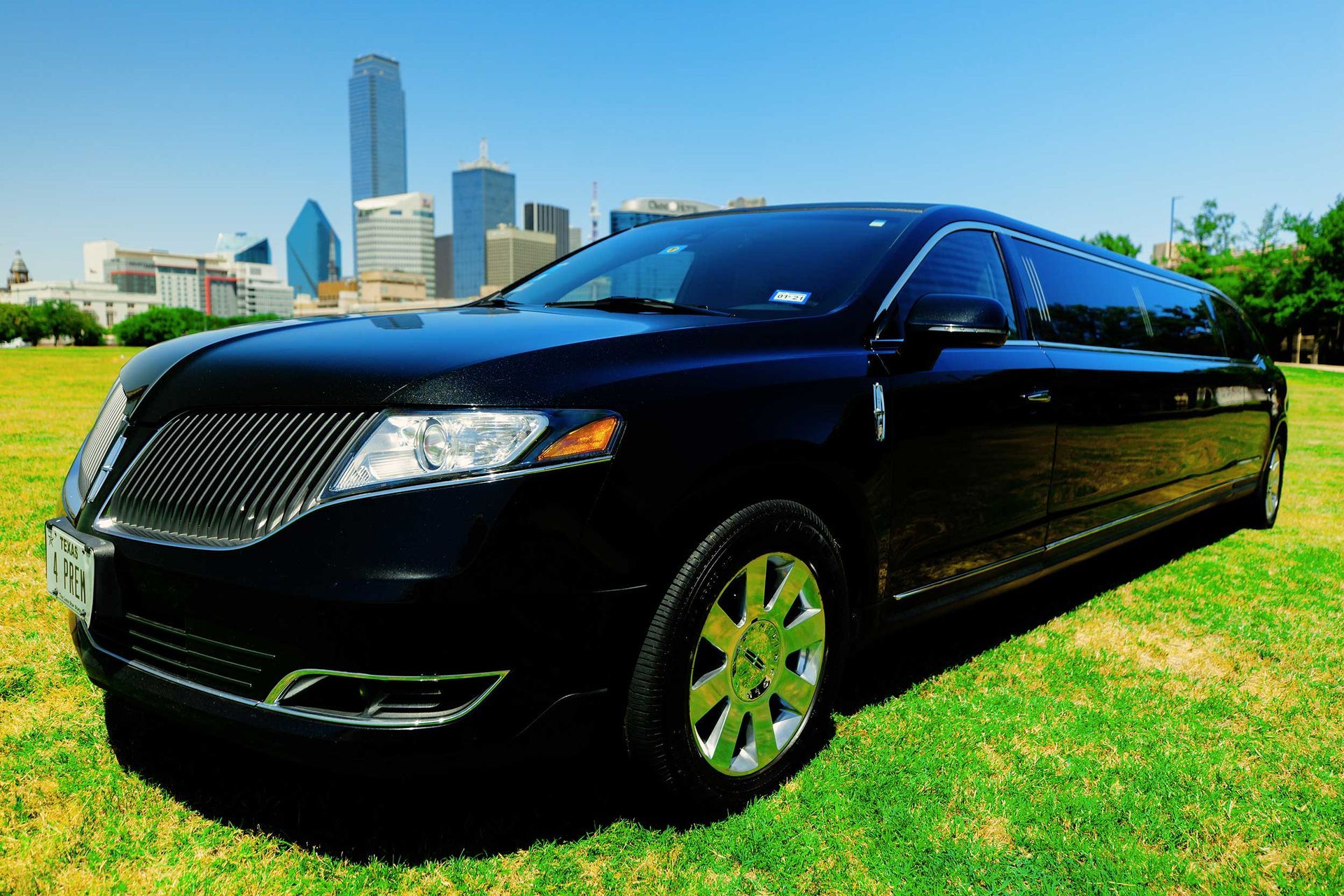 premier's black limousine is parked in a grassy field with a city skyline in the background