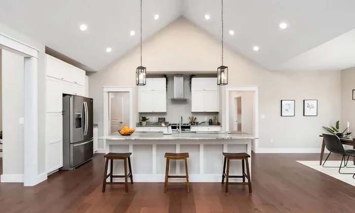 Open-concept kitchen with white cabinets, stainless steel appliances, a large island, and wood floors.