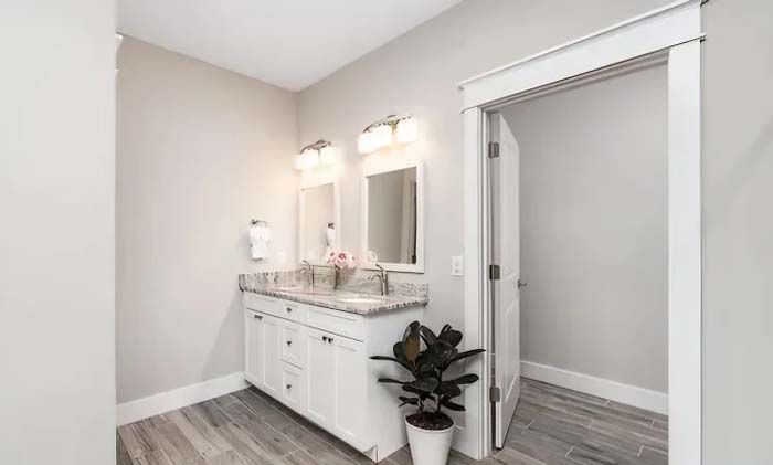 Bathroom with double vanity, two mirrors, and a door to a toilet. Light gray walls, white cabinets.