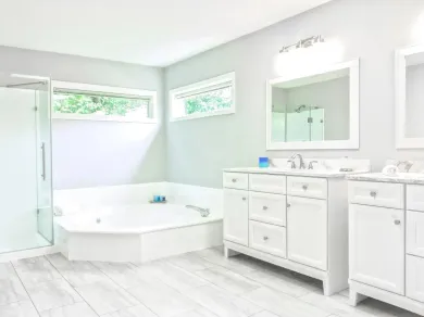 Bright white bathroom with a corner bathtub, double vanity, mirrors, and frosted windows