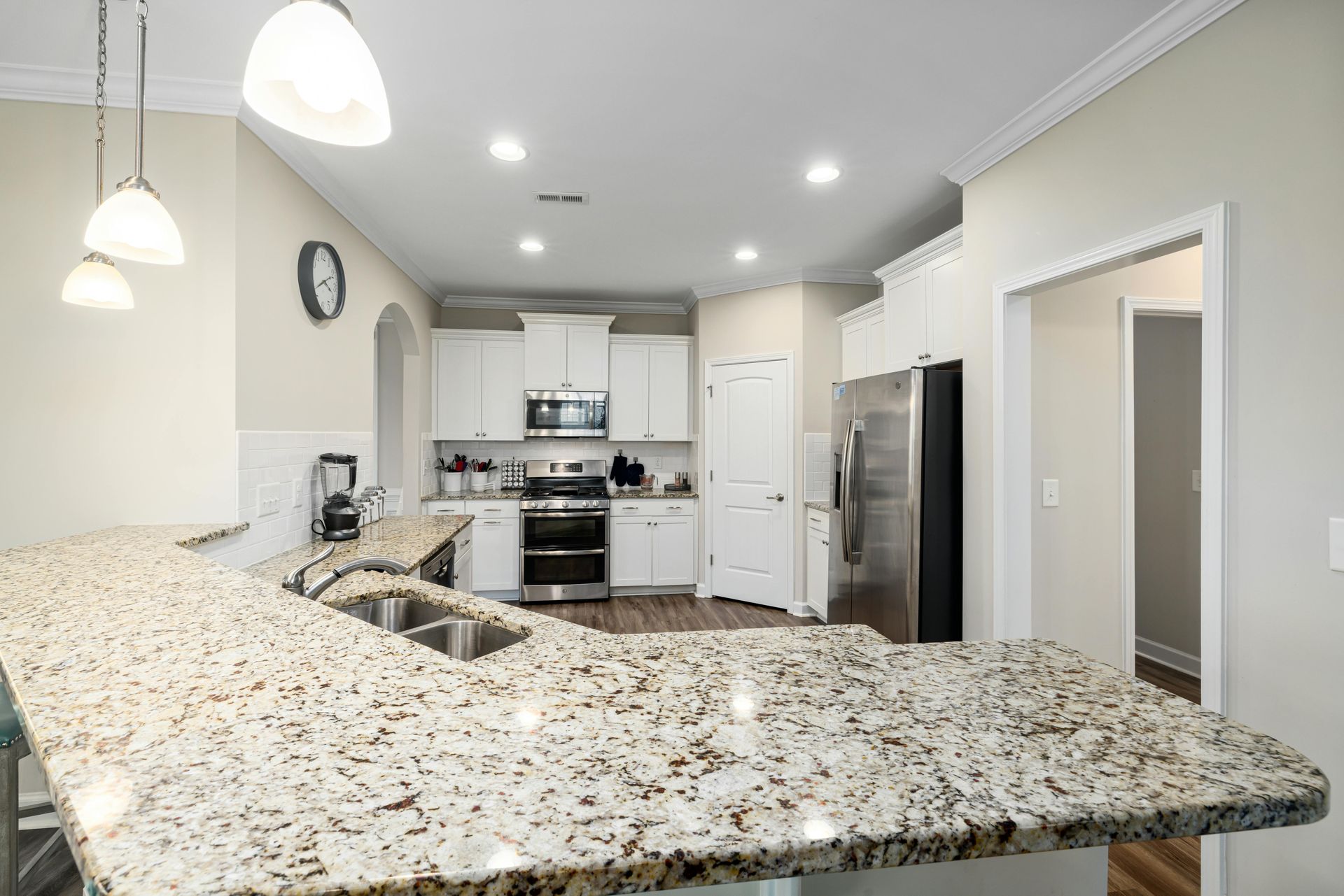 Bright modern kitchen with granite island, stainless steel appliances, white cabinets, and pendant lights