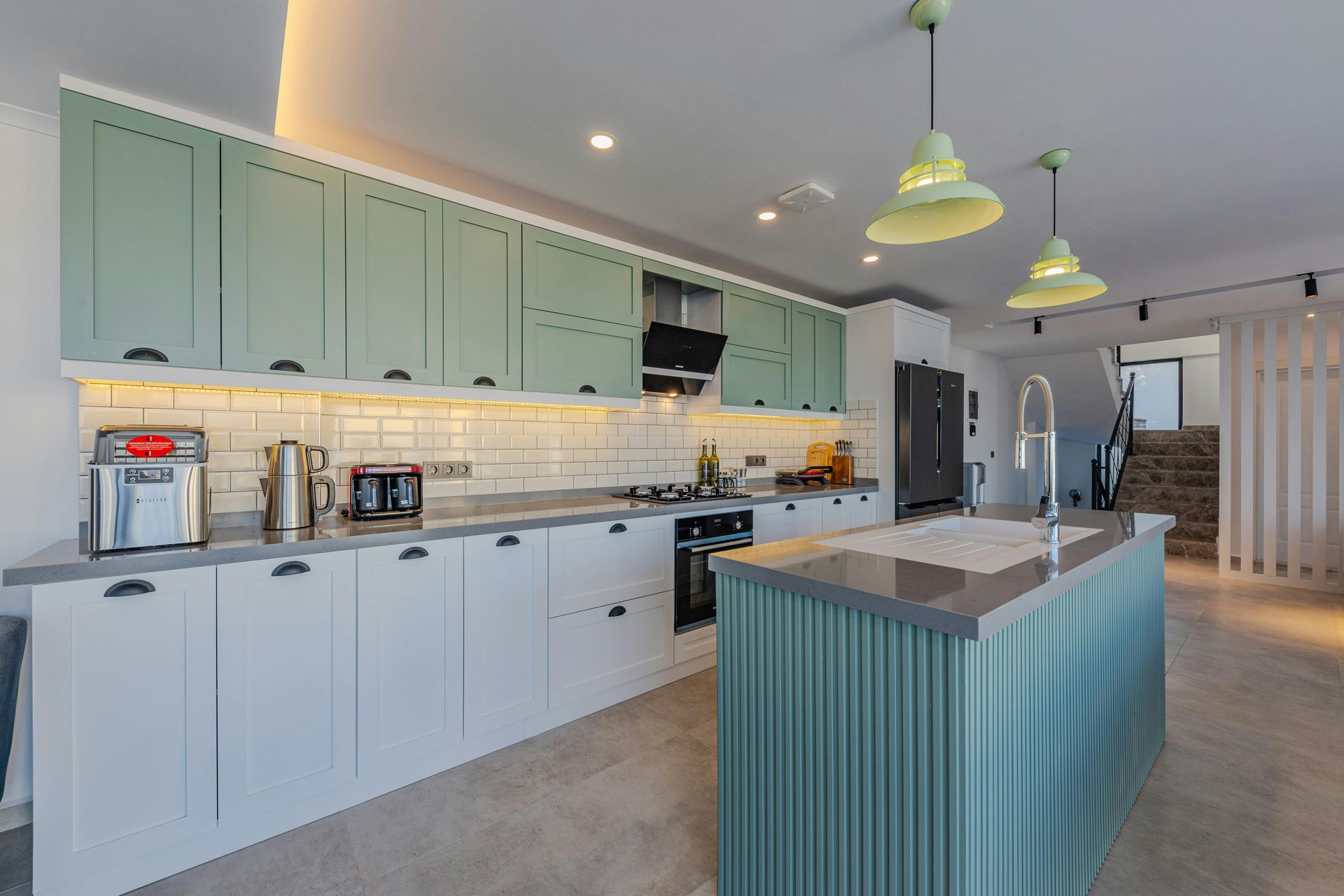 Modern kitchen with mint-green cabinets, white countertops, island, pendant lights, and built-in appliances