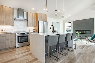 Modern kitchen with white island, gray stools, stainless appliances, and open living area with fireplace