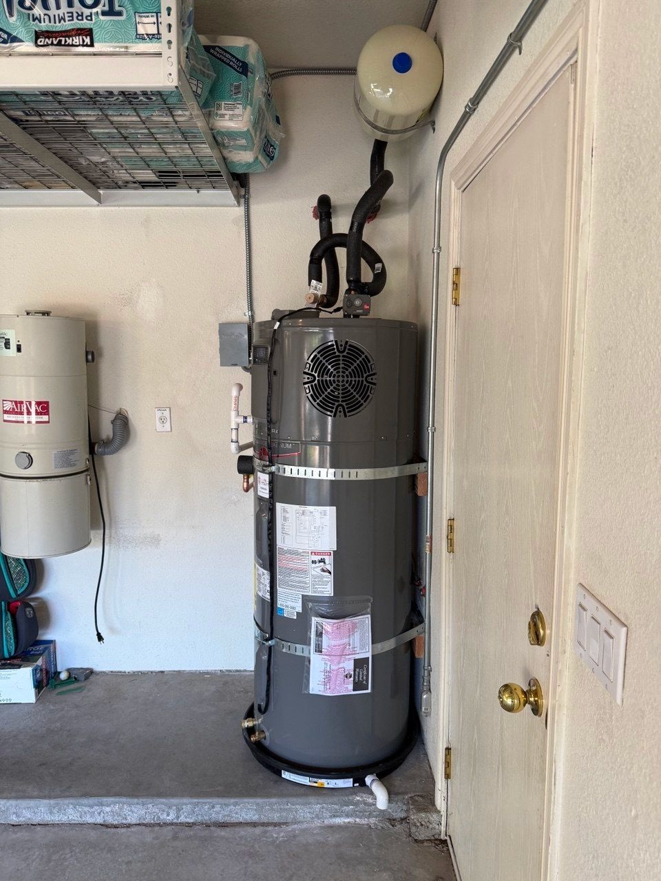 Laundry room with a silver water heater beside a black washer and wall shelves, labeled “After”