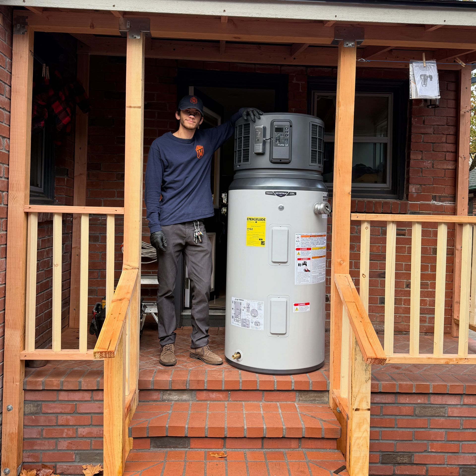 Man standing beside a large water heater on a brick porch