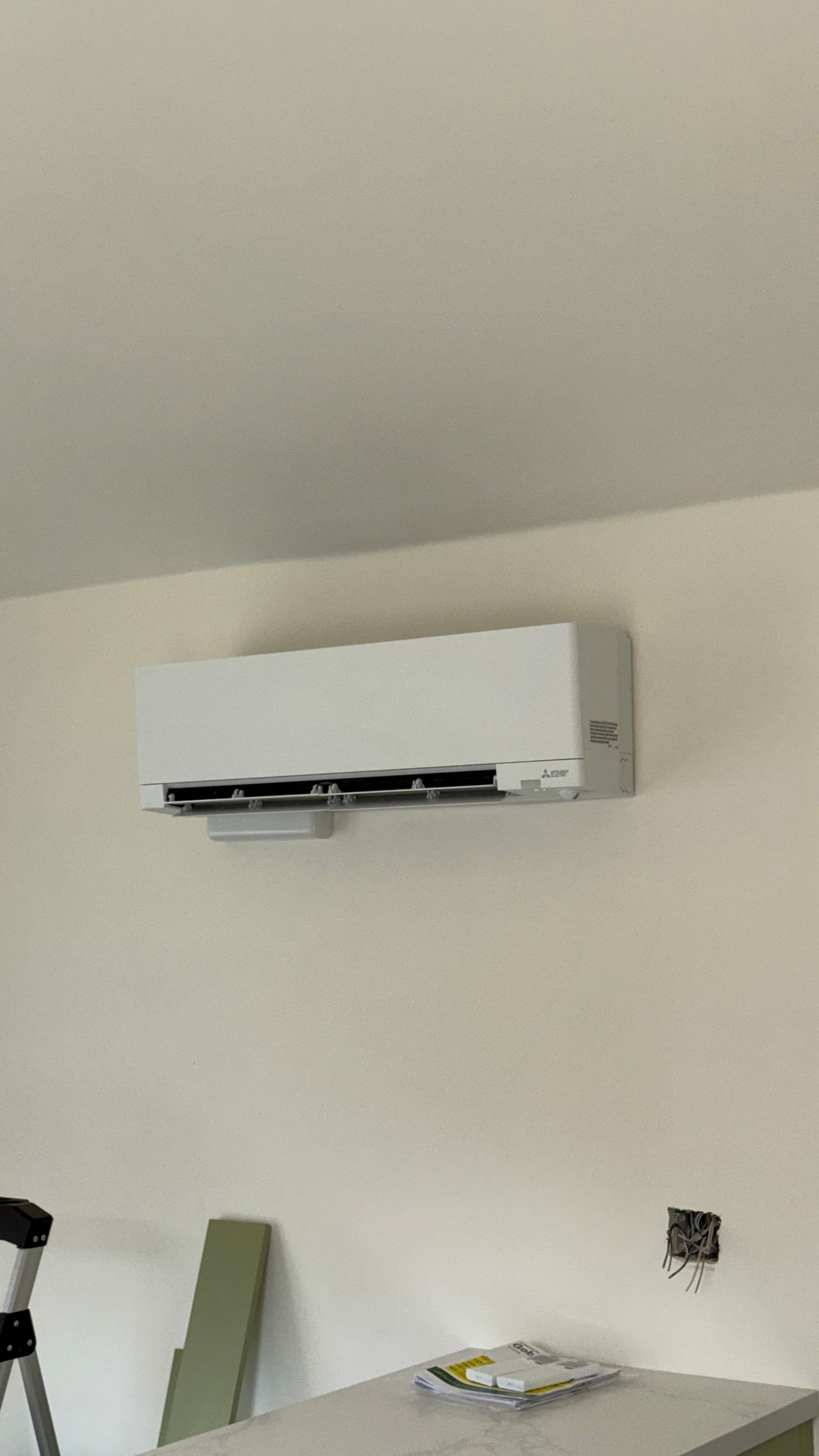 White wall-mounted air conditioner above a beige wall and shelf in a room