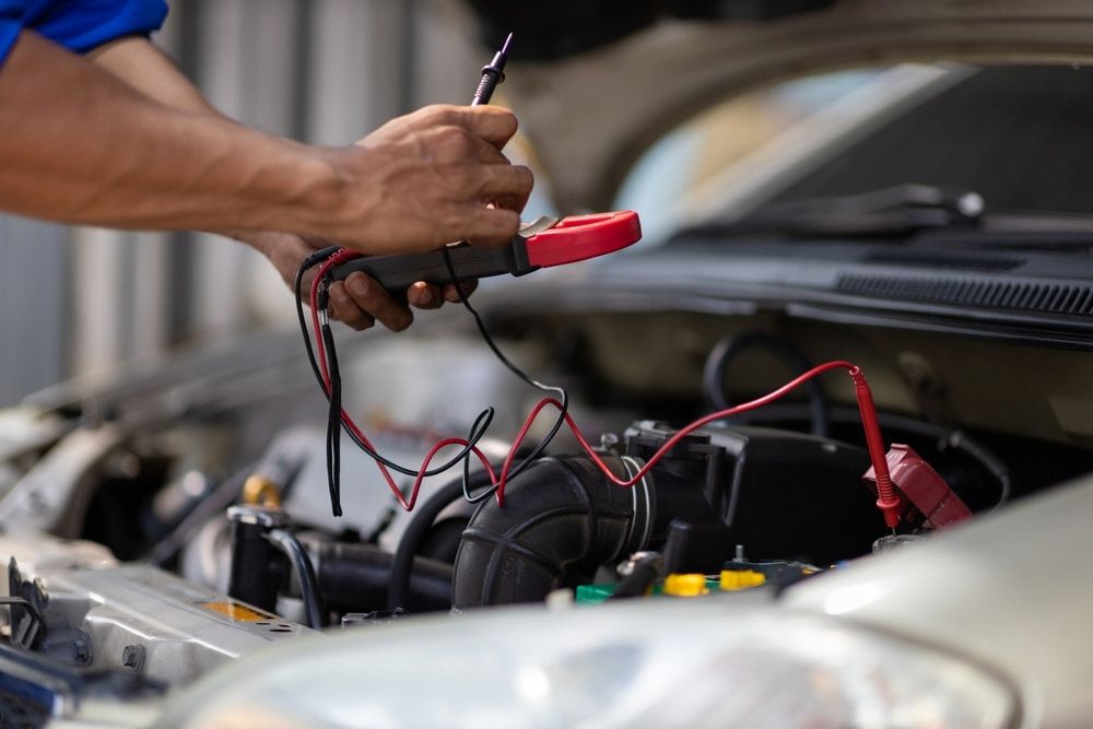 A Man is Working on the Engine of a Car With a Multimeter — Express Auto Repairs in Ainslie, ACT