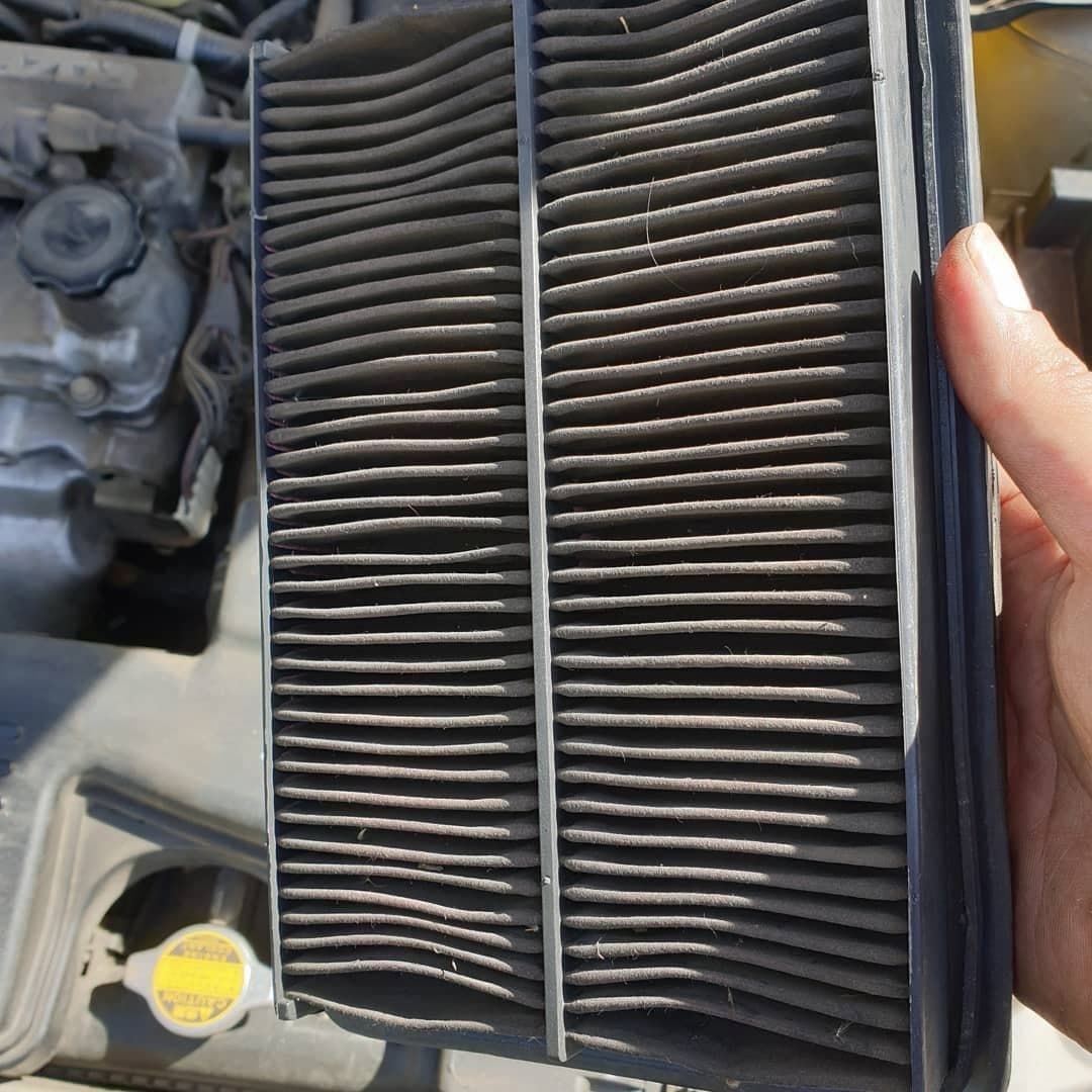A Person is Holding an Air Filter in Front of a Car Engine — Express Auto Repairs in Ainslie, ACT