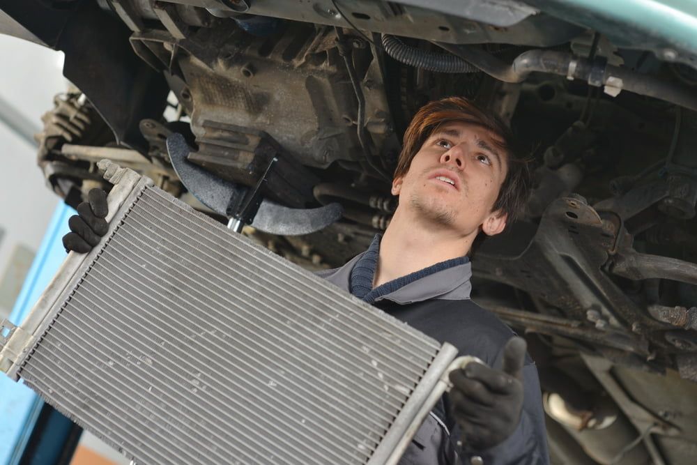 A Man is Holding a Radiator Under a Car — Express Auto Repairs in Ainslie, ACT