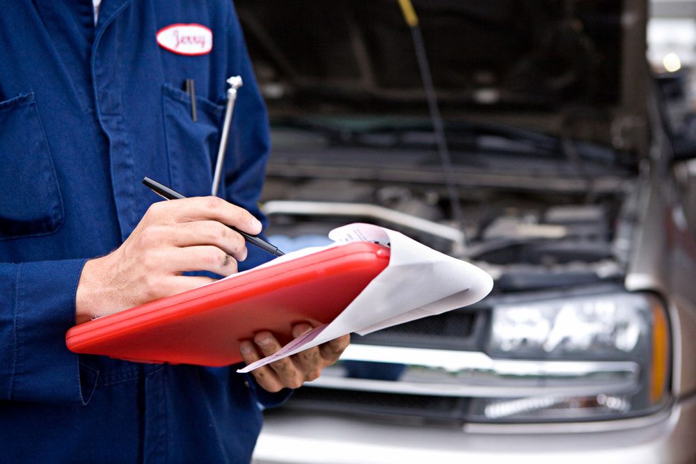 A Mechanic is Writing on a Clipboard in Front of a Car — Express Auto Repairs in Ainslie, ACT