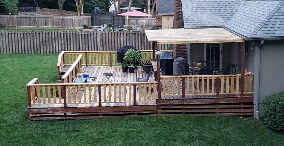 Wooden deck in a backyard with a grill, plants, and a partial awning.