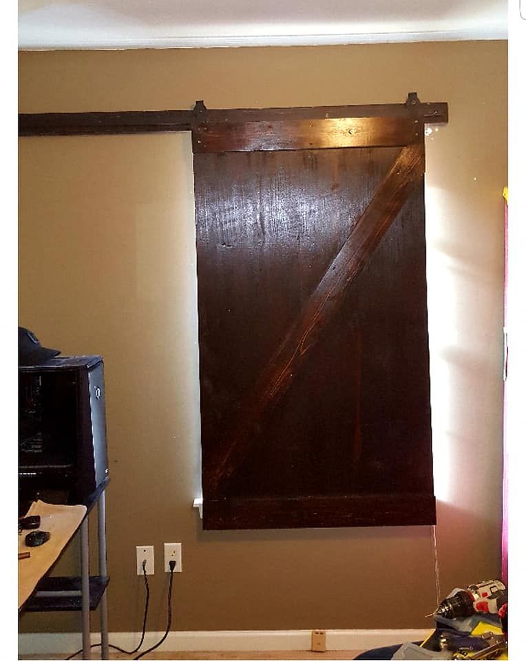 Wooden barn door, stained brown, slides on a rail above a tan wall, covering a window.