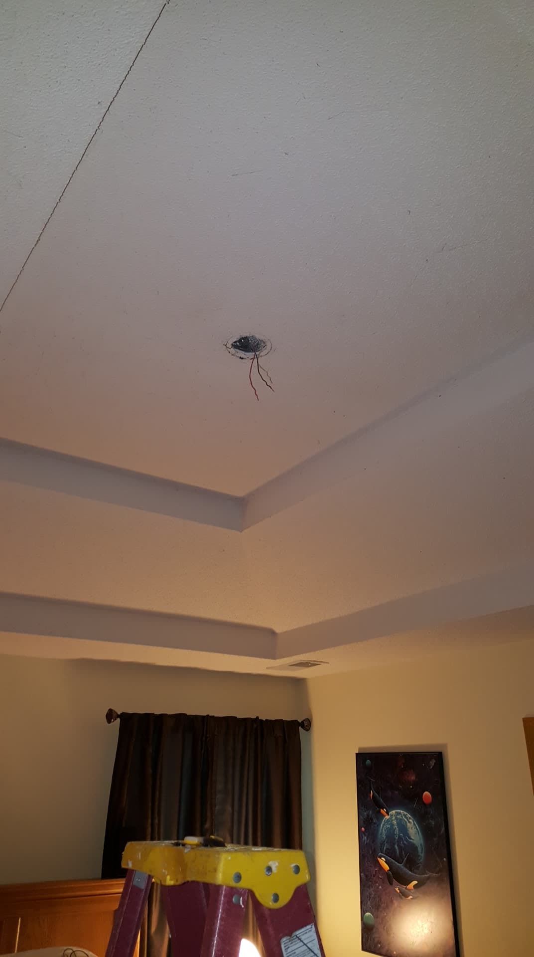 Ceiling with exposed wiring, light fixture. A stepladder and artwork below.