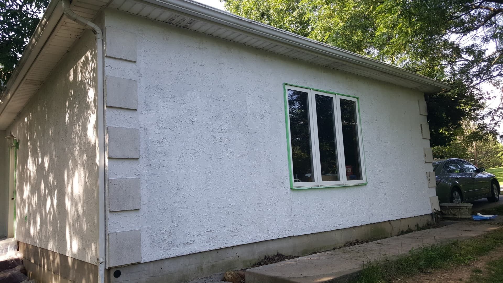 White stucco building with window and green trim; gray car parked nearby.
