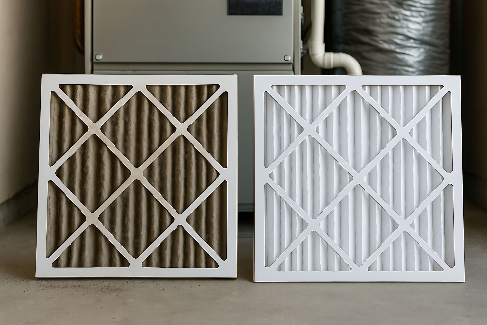 Dirty and clean air filters, side-by-side, in front of an HVAC unit. The dirty one is brown, the clean one white.