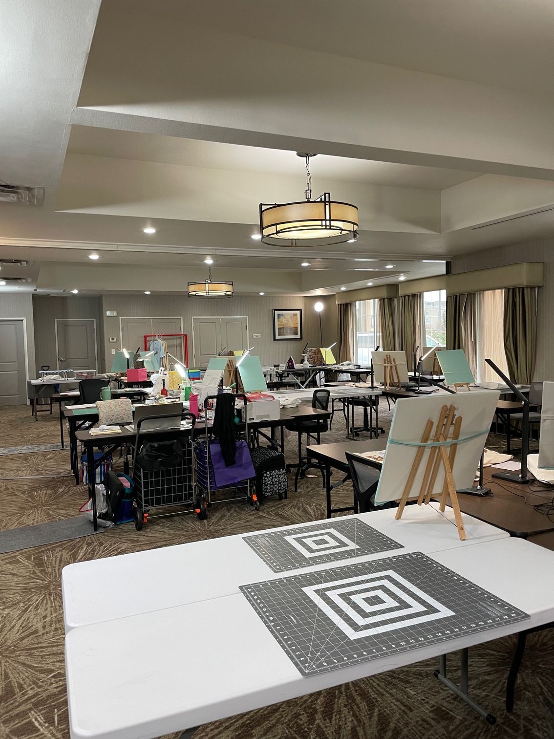 Craft room with tables, easels, and supplies. Beige walls, brown carpet, and neutral-toned furniture.