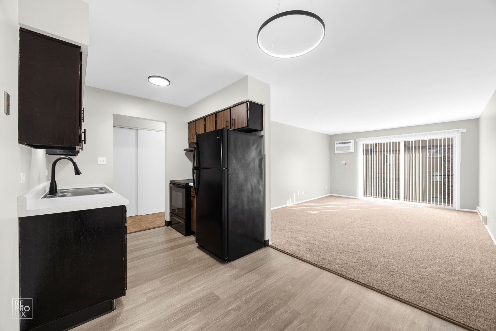 Kitchen with dark cabinets, black appliances, and living room with carpet and sliding door.