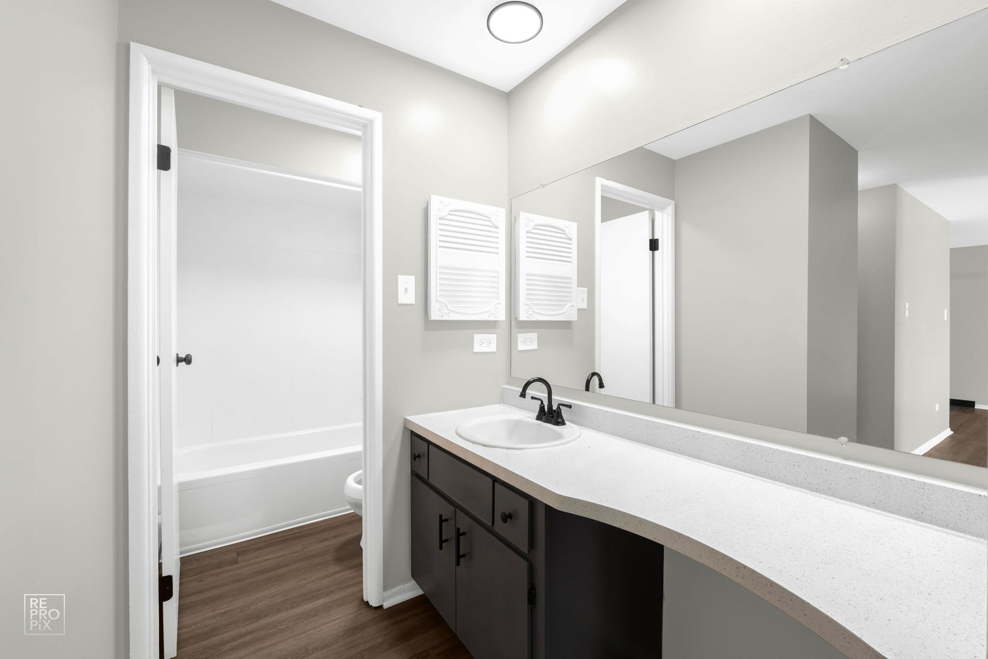 Bathroom with vanity, white countertop, dark cabinets, and mirror reflecting another doorway.