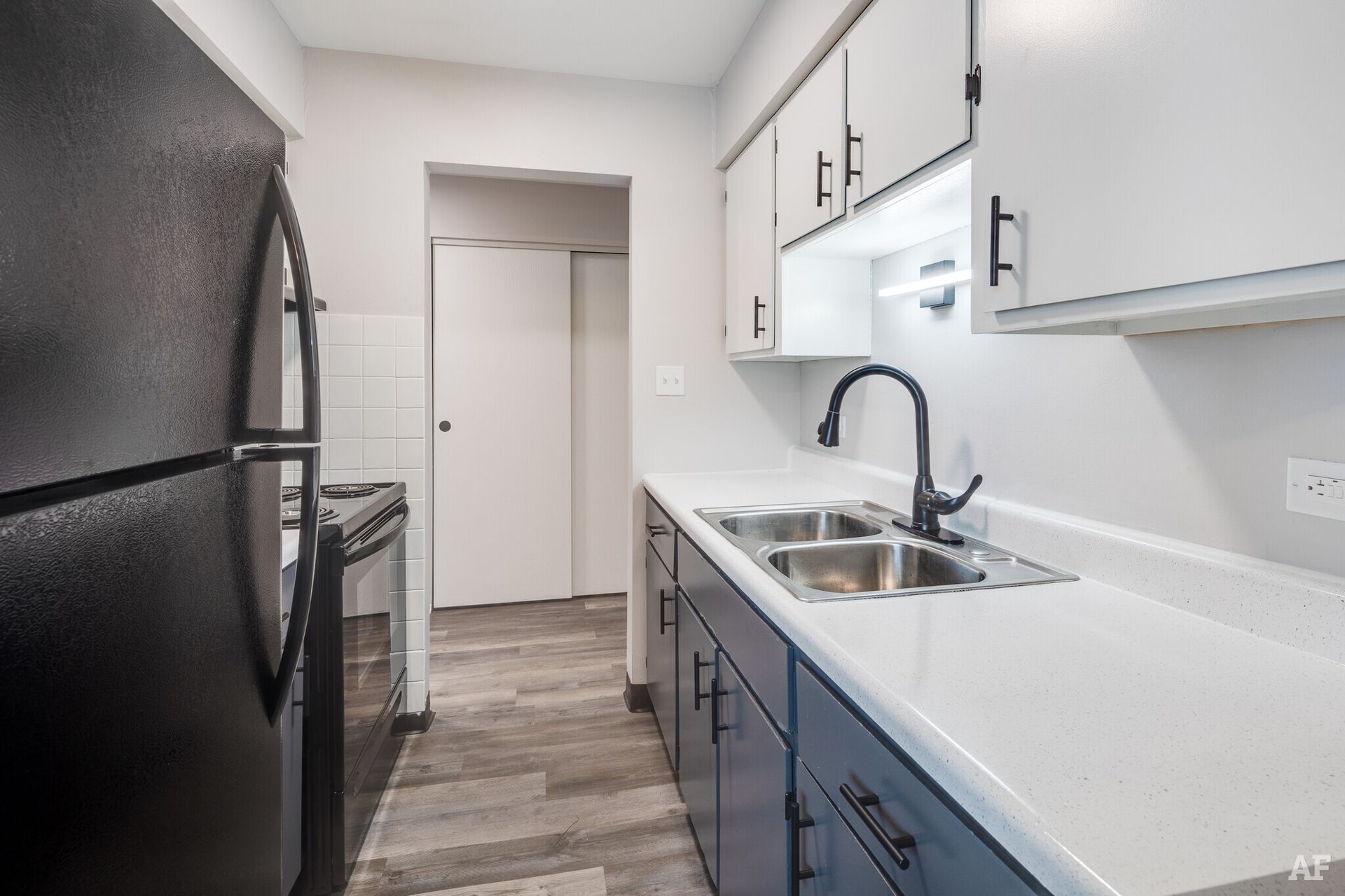 Kitchen with blue and white cabinets, stainless steel sink, and black refrigerator.
