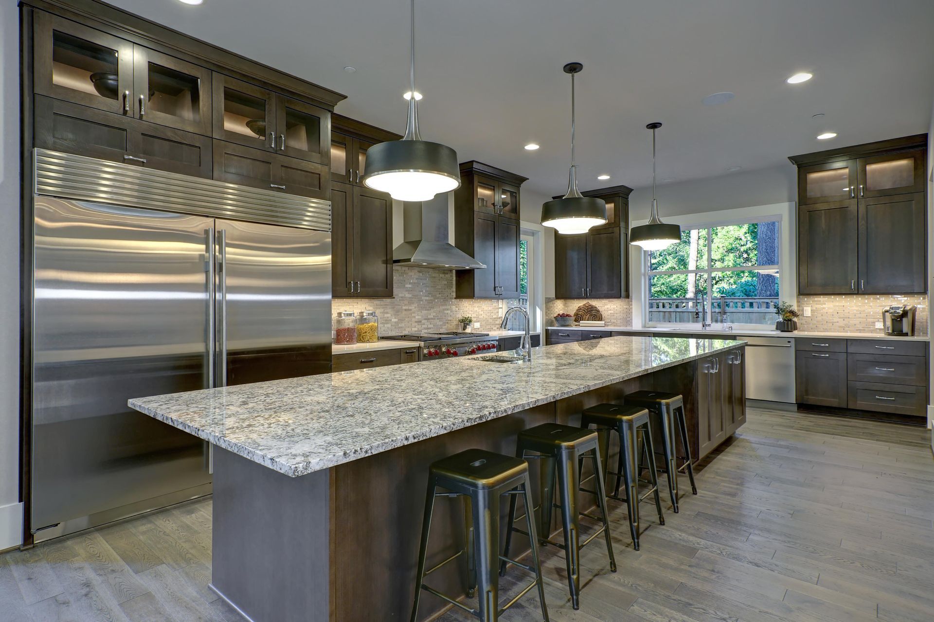 Modern kitchen with granite island, stainless steel appliances, dark cabinets, and pendant lights